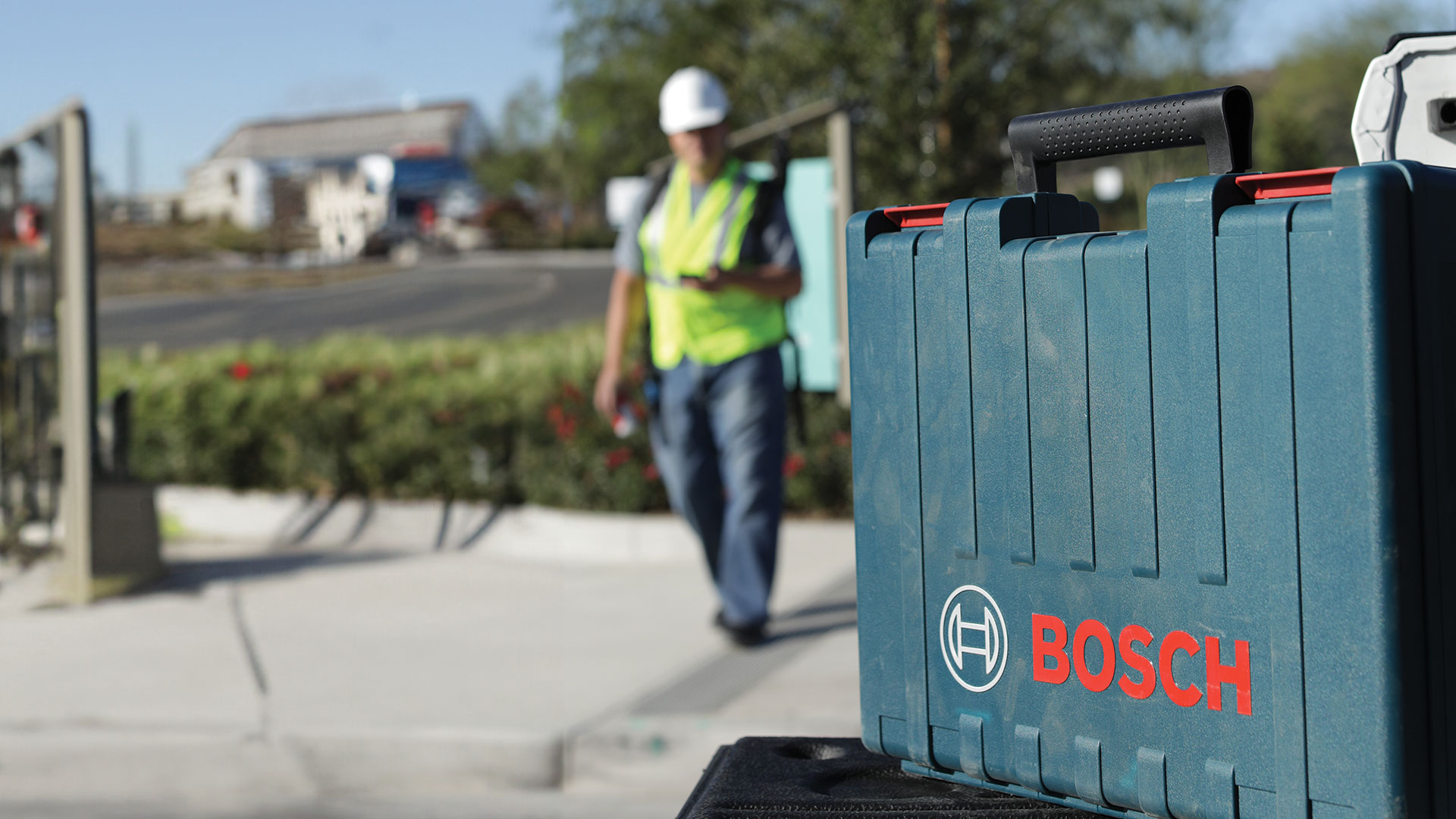 A green Bosch toolbox is on a table, workers in the background.